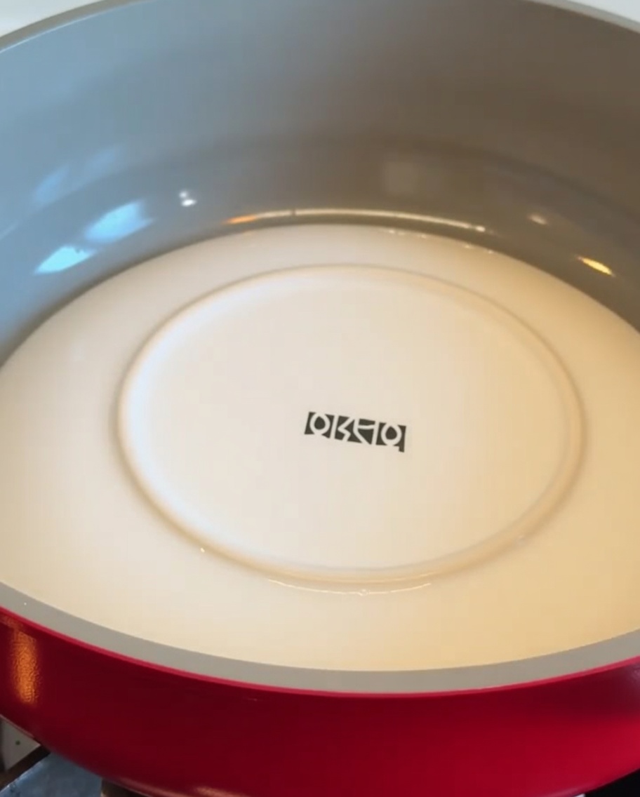 Un plato blanco colocado boca abajo dentro de una sartén roja para dar la vuelta a una base de patata.