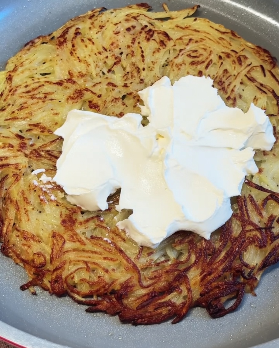 Queso crema blanco siendo puesto y alisado sobre la crujiente y caliente base de patata.