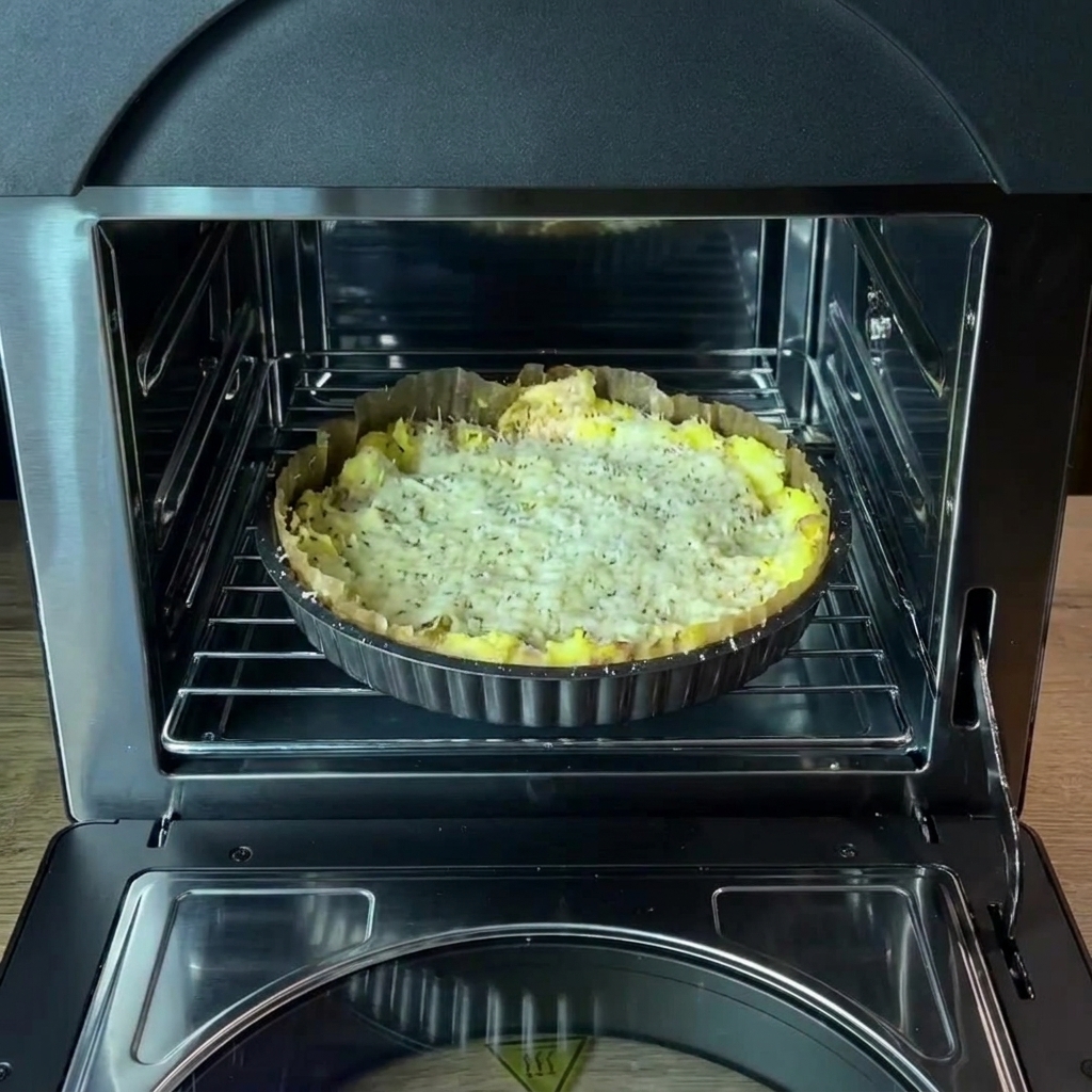 La bandeja de horno con la base de patata sazonada colocada en la rejilla interior del horno.
