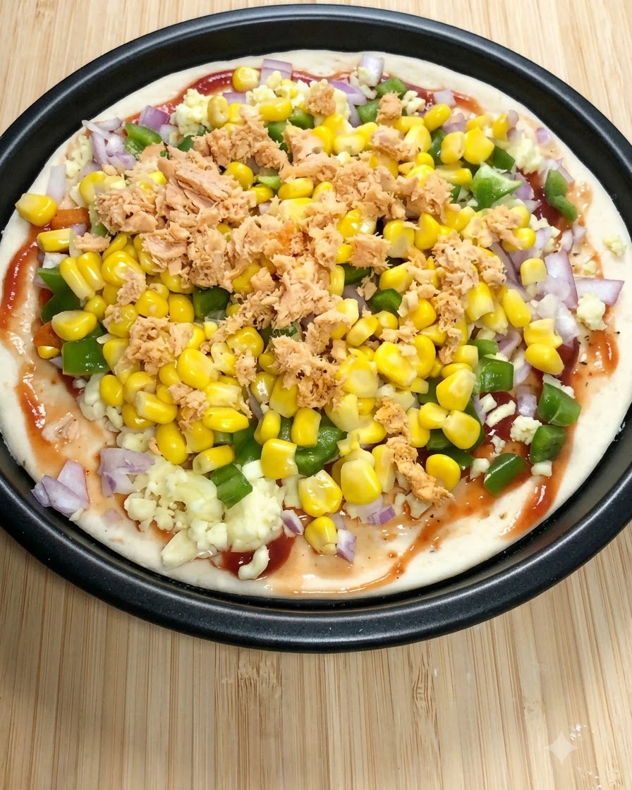Una base de pizza redonda cubierta con salsa de tomate, mozzarella, pimientos verdes, maíz dulce y trozos de salmón en lata.