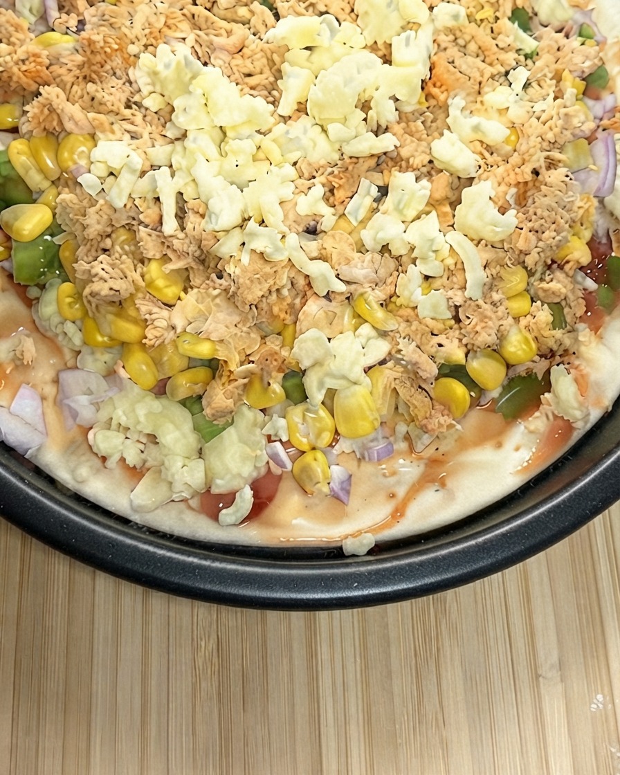 Vista de cerca de una pizza preparada siendo cubierta profusamente con una capa gruesa de queso mozzarella rallado.