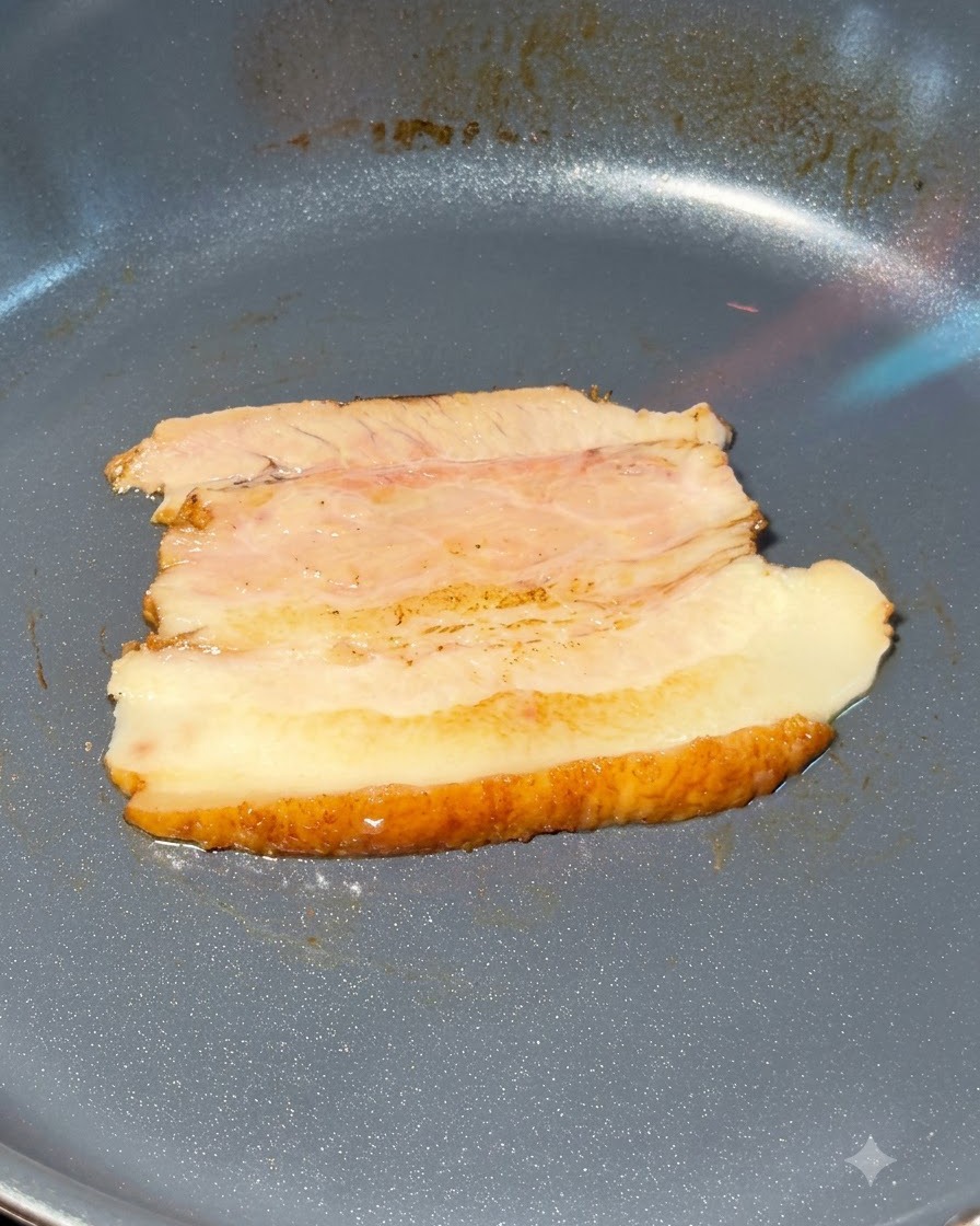 Rebanadas de panceta de cerdo chashu siendo flameadas con un soplete en una sartén.