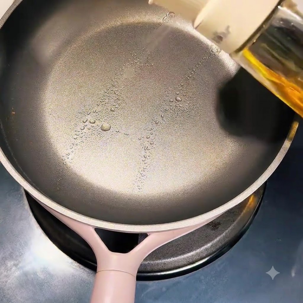 Una mano rociando aceite de cocina sobre la superficie de una sartén antiadherente limpia.