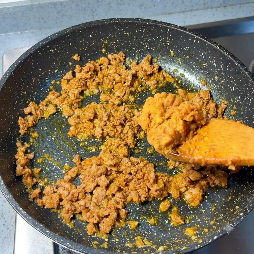Cucharada de pasta miso añadiéndose a la carne de cerdo picada en la sartén.