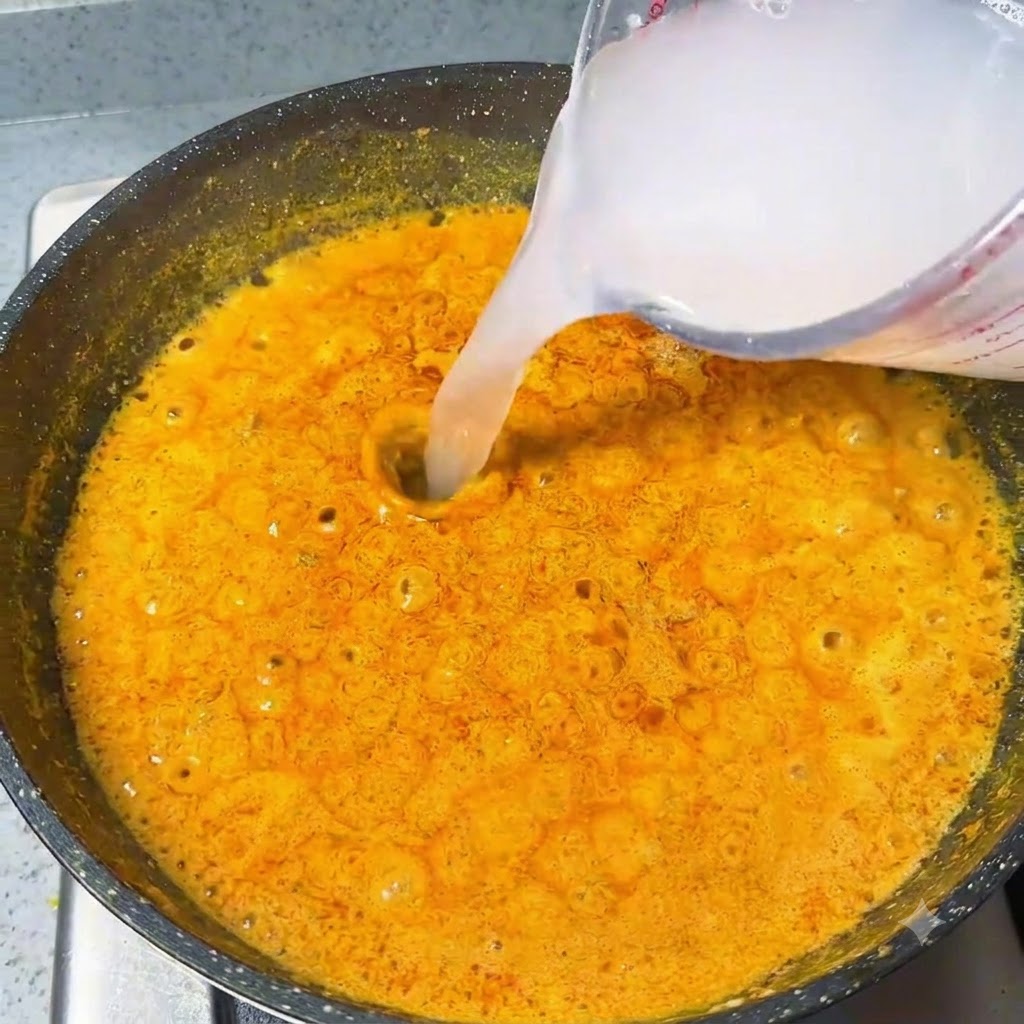 Agua vertiéndose desde una jarra medidora a una burbujeante salsa de curry naranja.