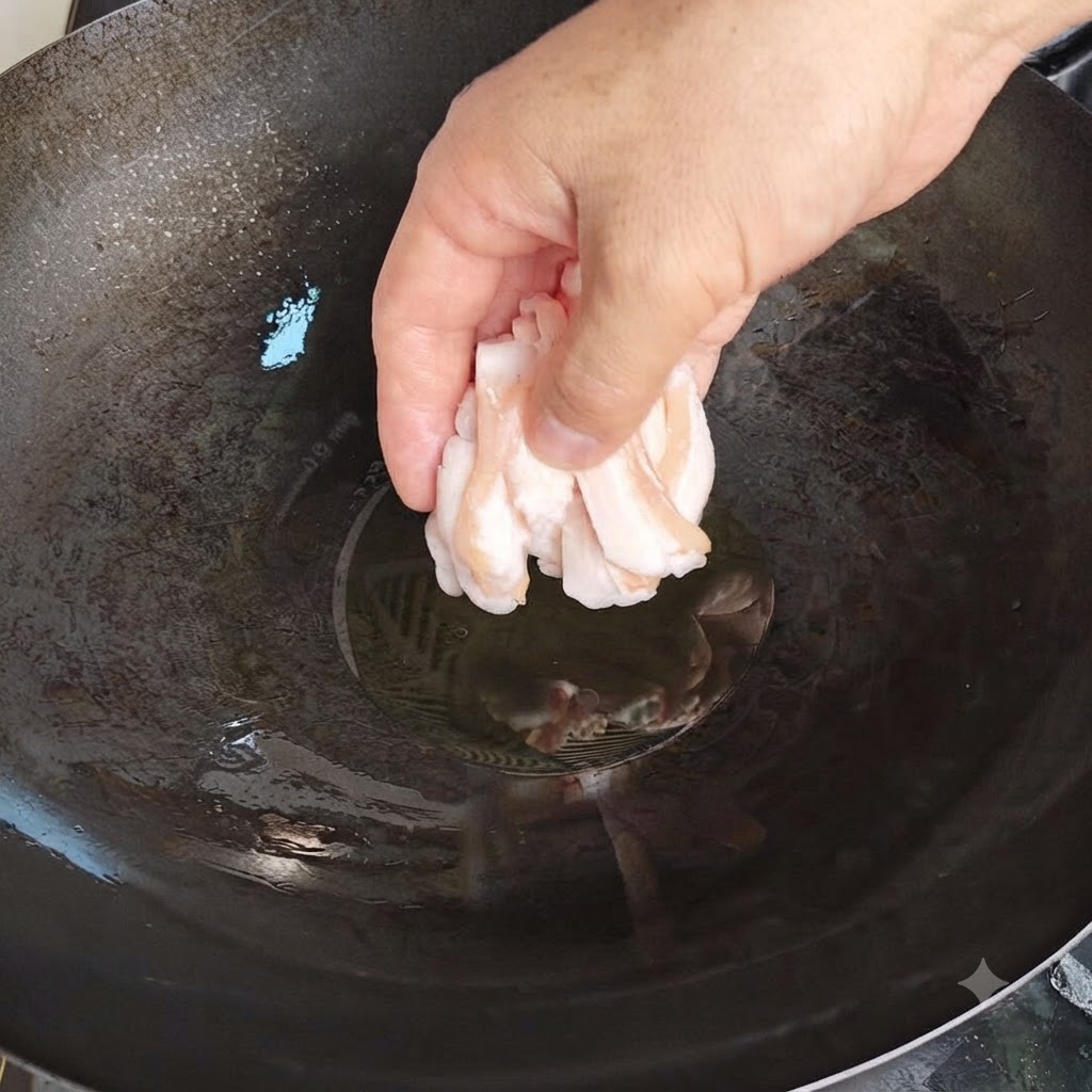 Una mano colocando cuidadosamente finas rodajas de grasa de cerdo cruda en un wok caliente con aceite.