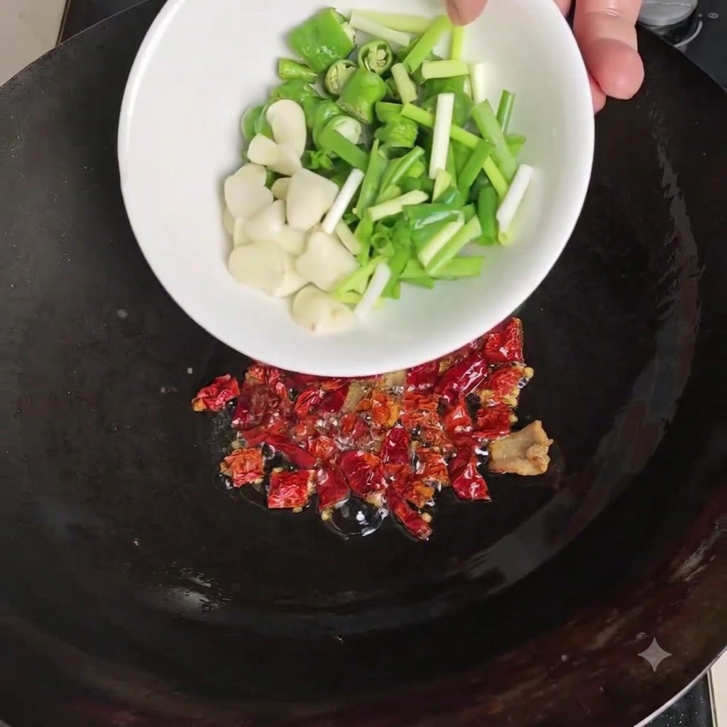 Un tazón blanco virtiendo chiles verdes en rodajas, ajo pelado y cebollines sobre los chiles secos tostados en el wok.