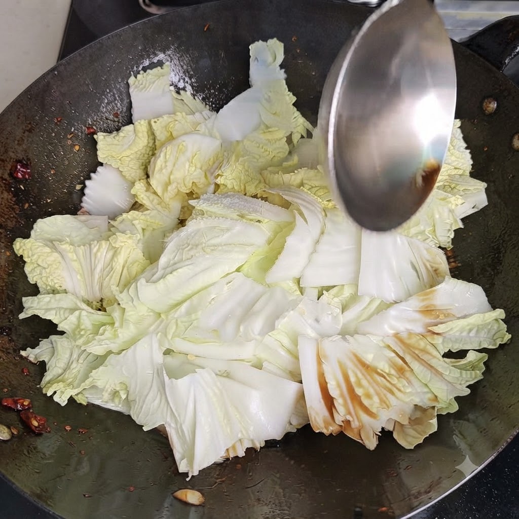 Una espátula de wok de metal removiendo y salteando repollo chino y condimentos vigorosamente dentro de un wok caliente.