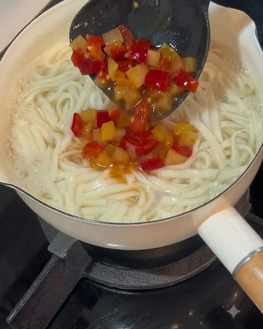 Un cucharón vertiendo la base de sopa de chile encurtido sobre una olla de fideos cocidos.