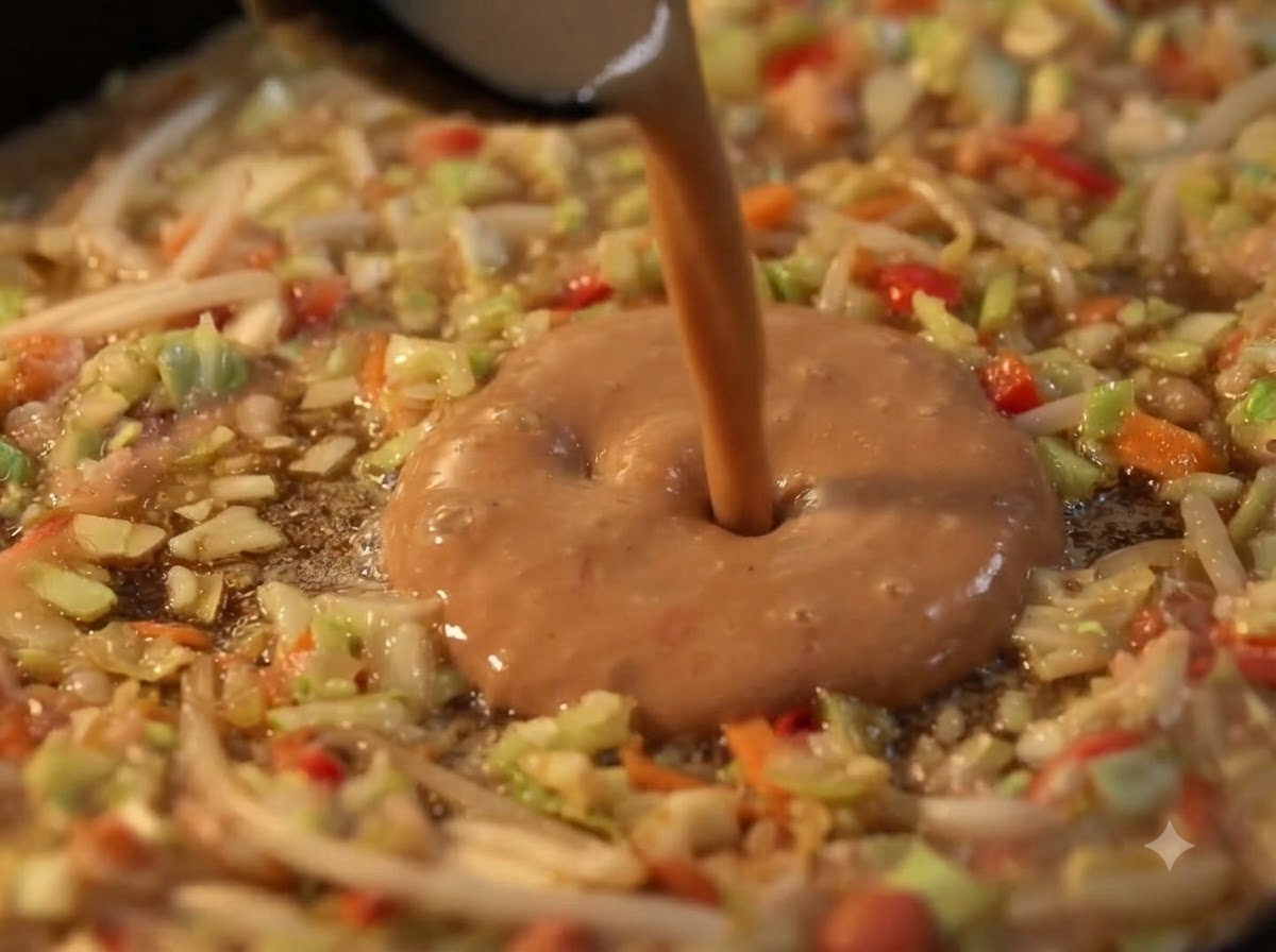 Masa líquida siendo vertida en el centro hueco de un anillo de verduras en una plancha caliente.