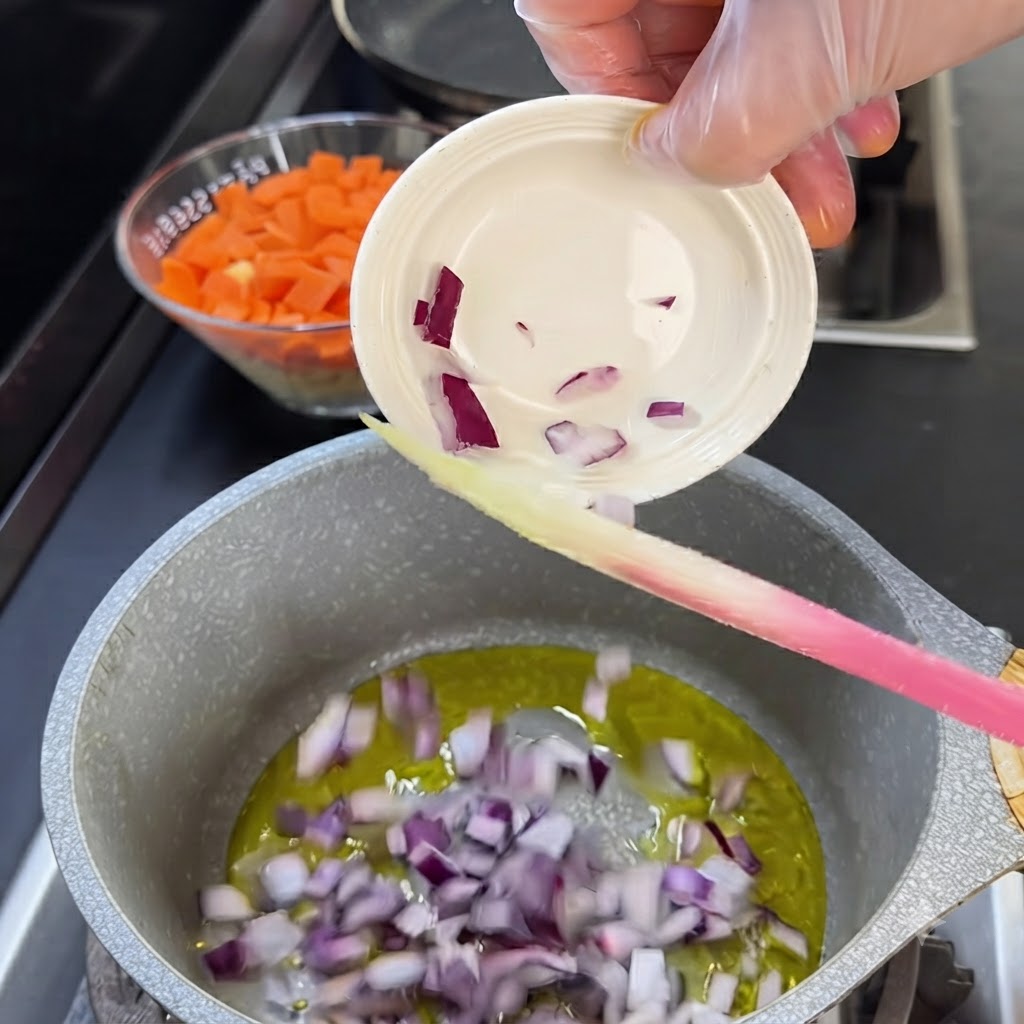 Trozos de cebolla roja siendo vertidos desde un pequeño cuenco blanco en una olla con aceite caliente.