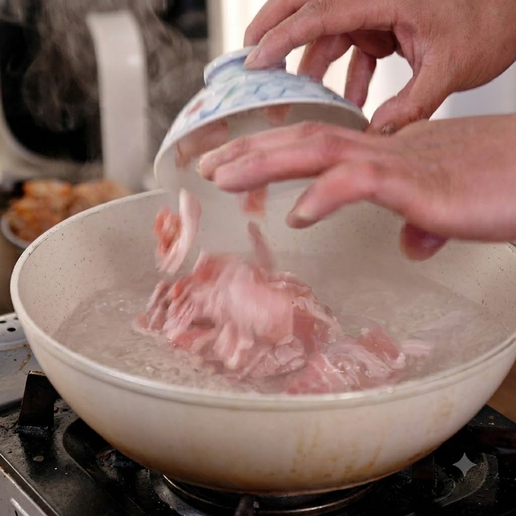 Manos dejando caer rodajas de panceta de cerdo cruda desde un pequeño bol de cerámica en una sartén con agua hirviendo activamente.