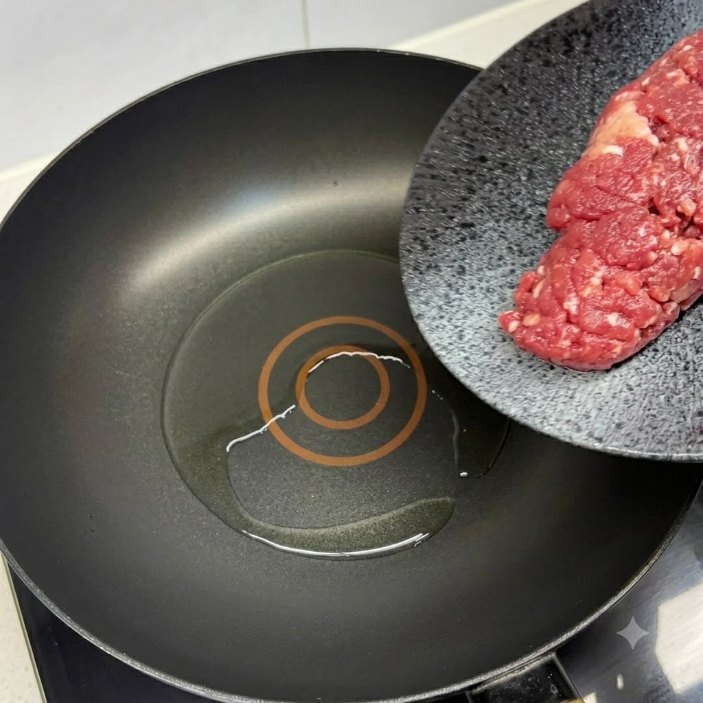 Carne picada de res fresca siendo añadida a una sartén negra caliente con aceite y una espátula roja.