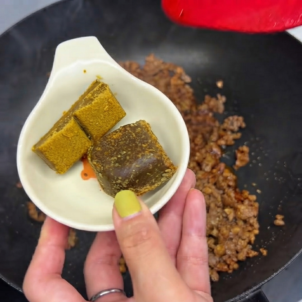 Dos bloques de curry sostenidos en un pequeño plato blanco listos para ser arrojados a la sartén con carne picada.
