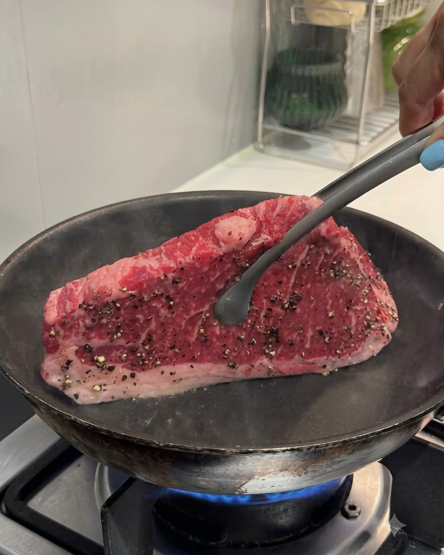 Pinzas sosteniendo un filete en posición vertical contra una sartén caliente para sellar el borde.