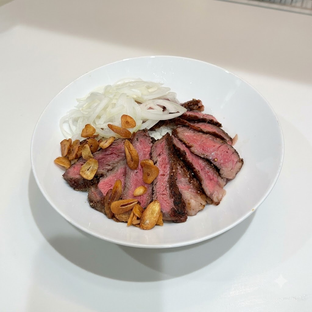 Un bol blanco que contiene filete cortado, cebollas cortadas y una dispersión de chips de ajo crujientes de color marrón dorado sobre el arroz.