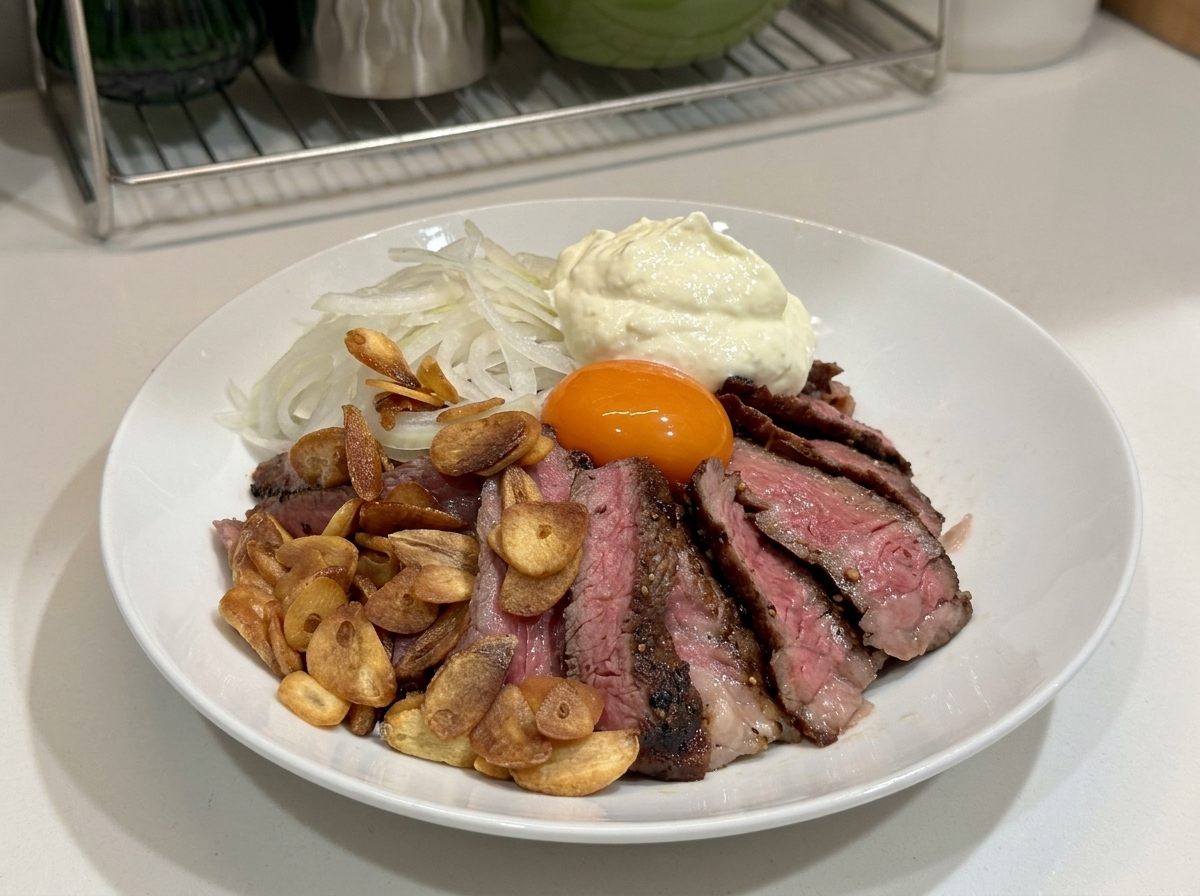 Un bol blanco lleno de filete cortado, chips de ajo, cebollas, una yema de huevo y una gran porción de nata montada encima.
