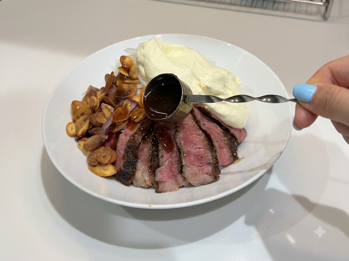 Una mano usando un pequeño medidor con asa para rociar salsa teriyaki oscura y brillante sobre un bol de arroz con filete completado.
