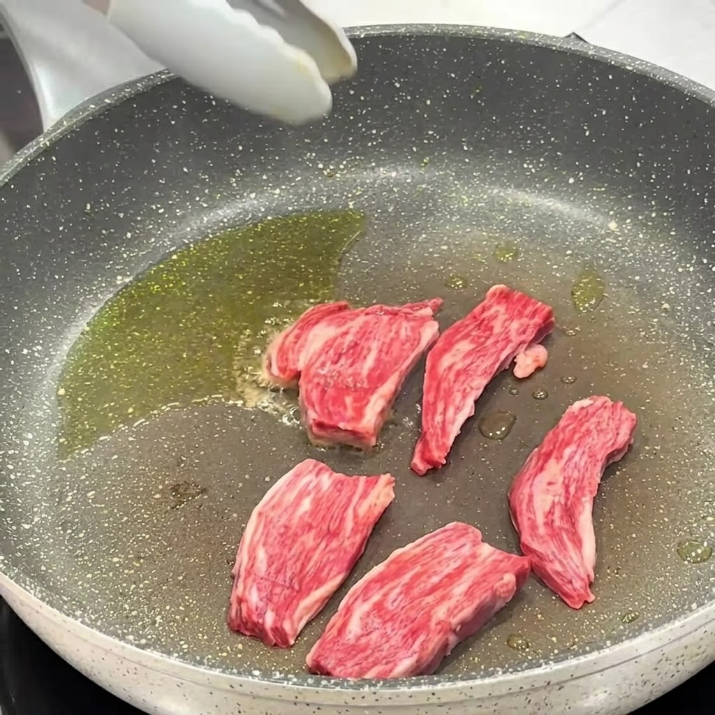 Sal y pimienta negra siendo esparcidas sobre los trozos de bistec que se cocinan en la sartén.