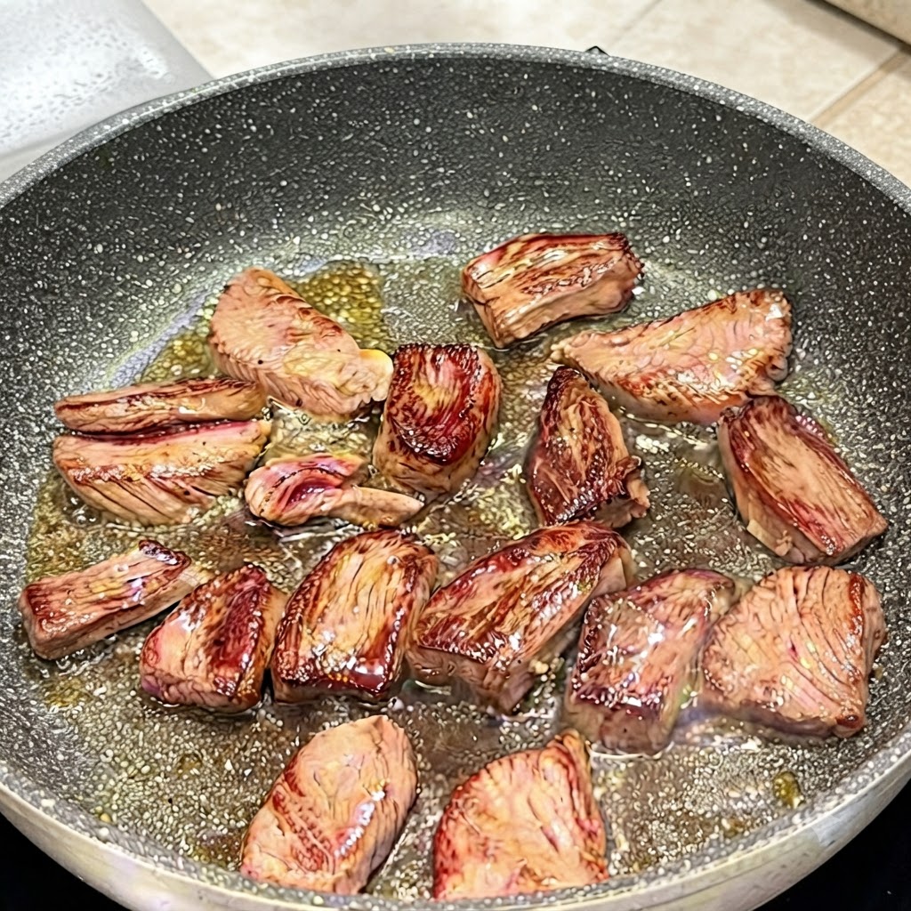Pinzas volteando los trozos de bistec de falda en una sartén para mostrar las superficies doradas.