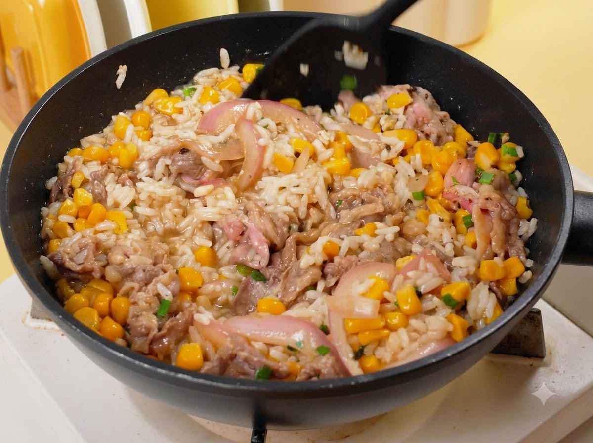 Una espátula negra mezclando arroz, ternera, maíz y cebollas en una sartén al fuego.