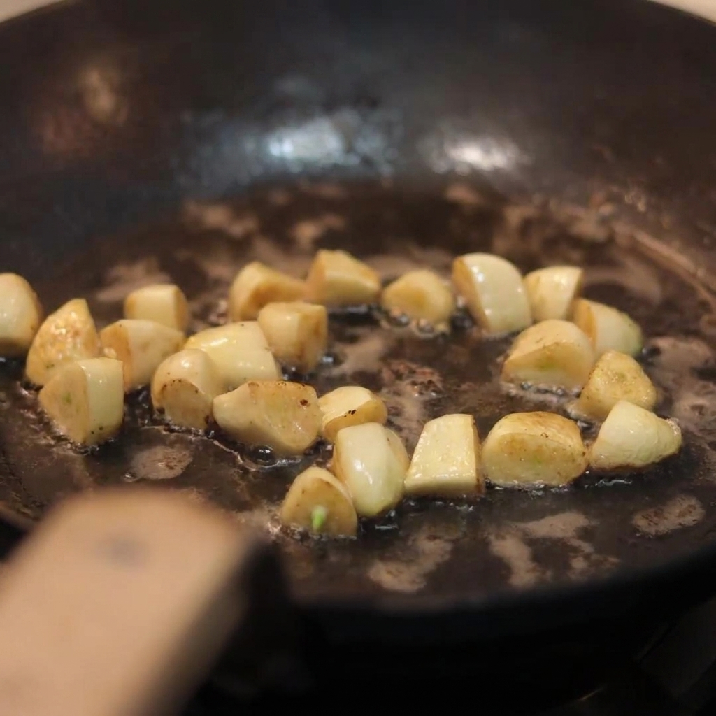 Champiñones blancos en láminas añadiéndose a una sartén que contiene los dientes de ajo dorados.