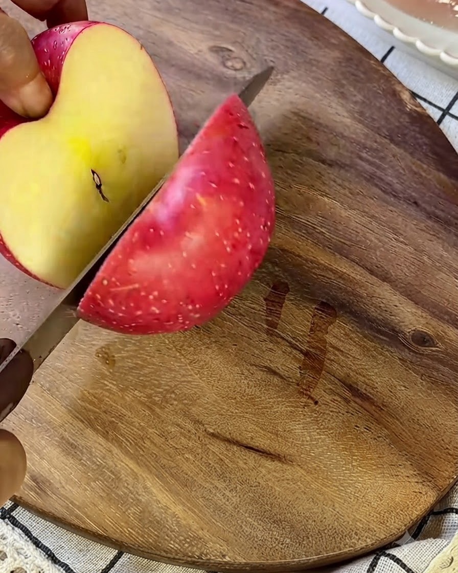 Una manzana siendo cortada en trozos pequeños sobre una tabla de madera con un cuchillo plateado.