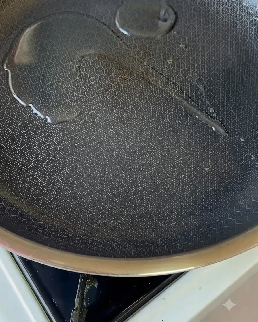Un pequeño charco de aceite brillando dentro de una sartén antiadherente caliente sobre la estufa.
