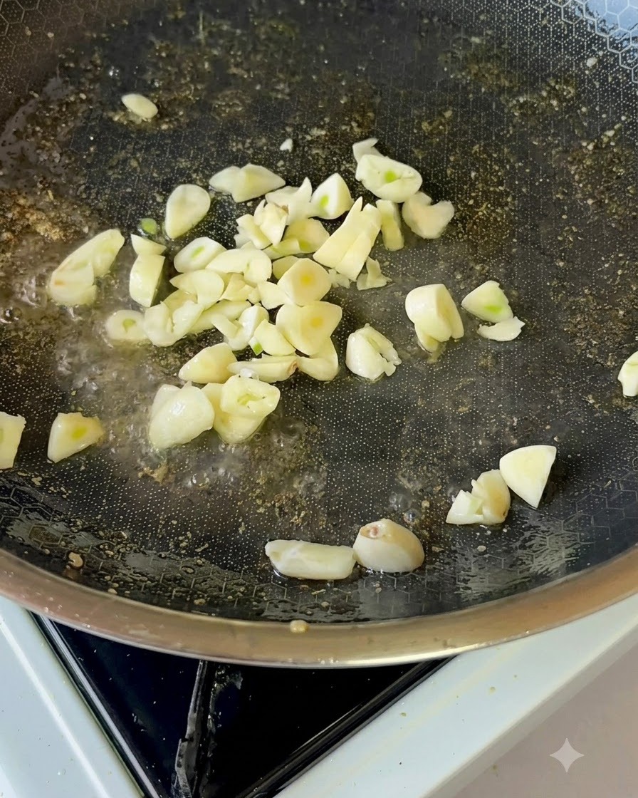 Rodajas de ajo fresco friéndose suavemente en aceite dentro de una sartén antiadherente.