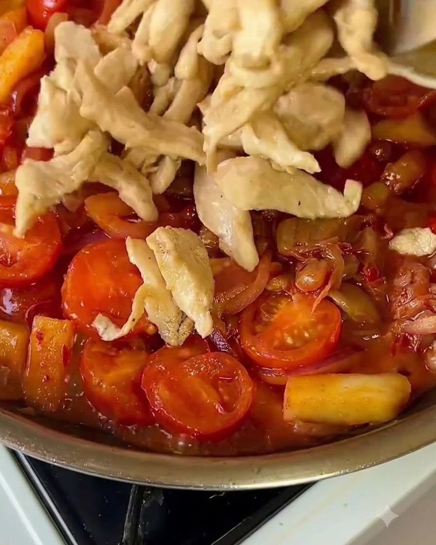 Tiras de pollo cocinadas siendo devueltas a una sartén vibrante llena de verduras.
