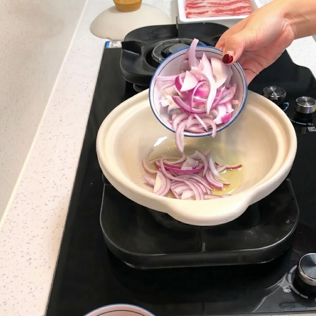 Rodajas de cebolla roja y trozos de tomate pelado siendo vertidos desde un tazón pequeño en una olla de barro caliente con aceite.