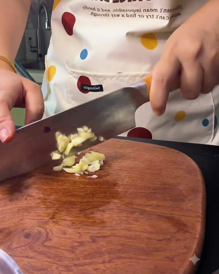 Dientes de ajo siendo picados finamente con un cuchillo de cocina en una tabla de madera.