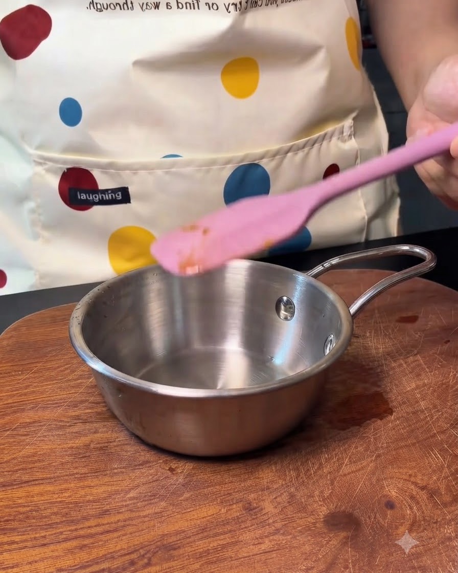 Una pequeña olla de metal vacía con una espátula de silicona rosa reposando cerca.