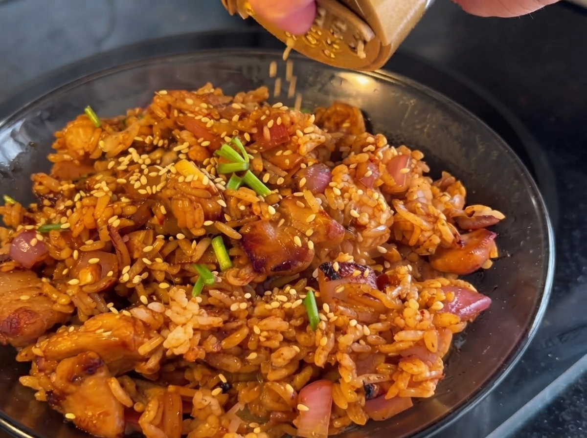 Kimchi siendo añadido a la sartén y salteado junto con el pollo y las cebollas.