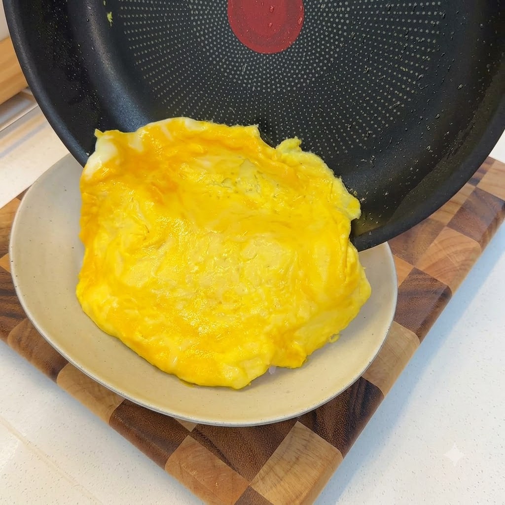 Una tortilla suave cocida deslizándose fuera de una sartén y cubriendo una porción de arroz blanco.
