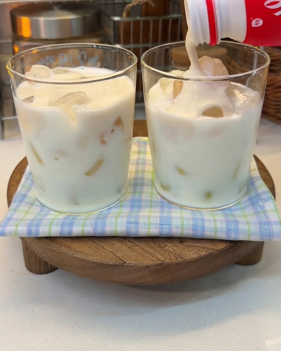 Yogur espeso siendo vertido desde una botella en un vaso de leche con hielo.