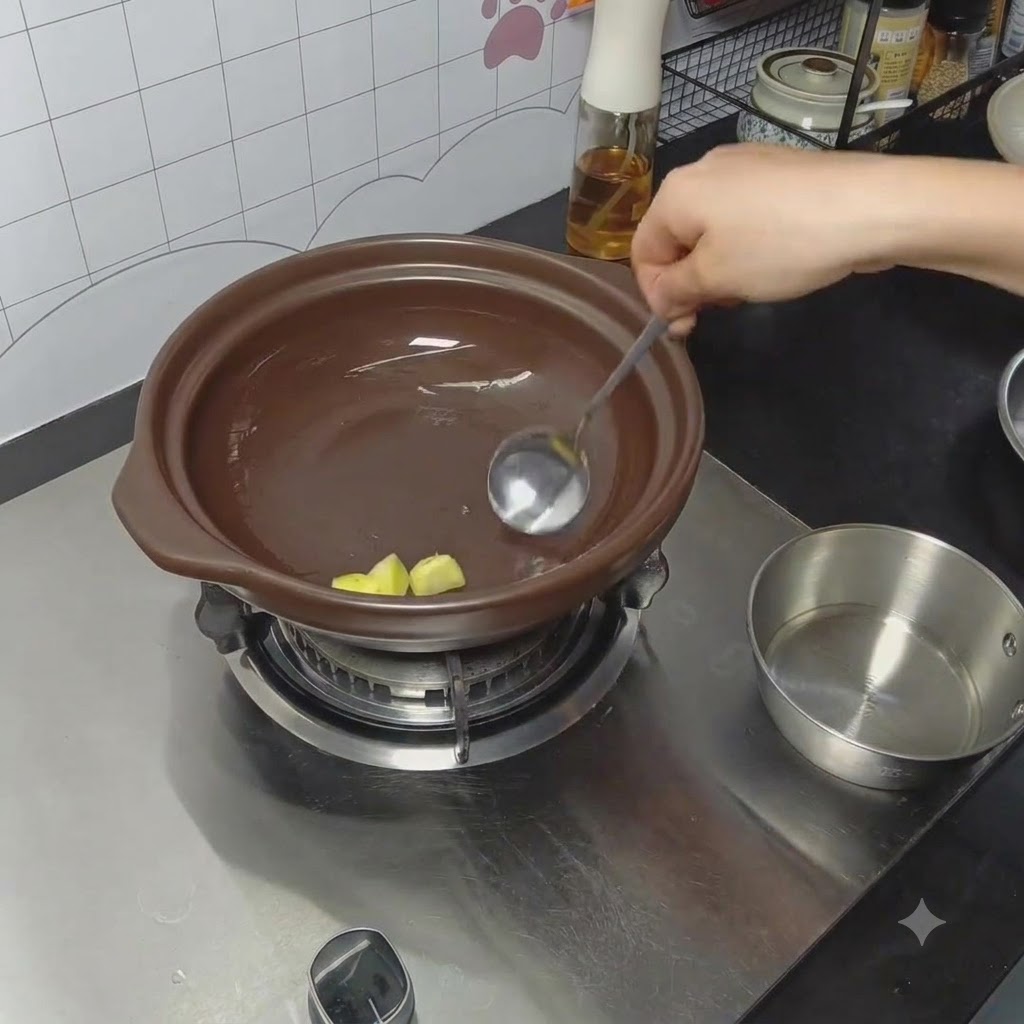 Jengibre siendo frotado con aceite en el fondo de una cazuela de barro usando una cuchara.