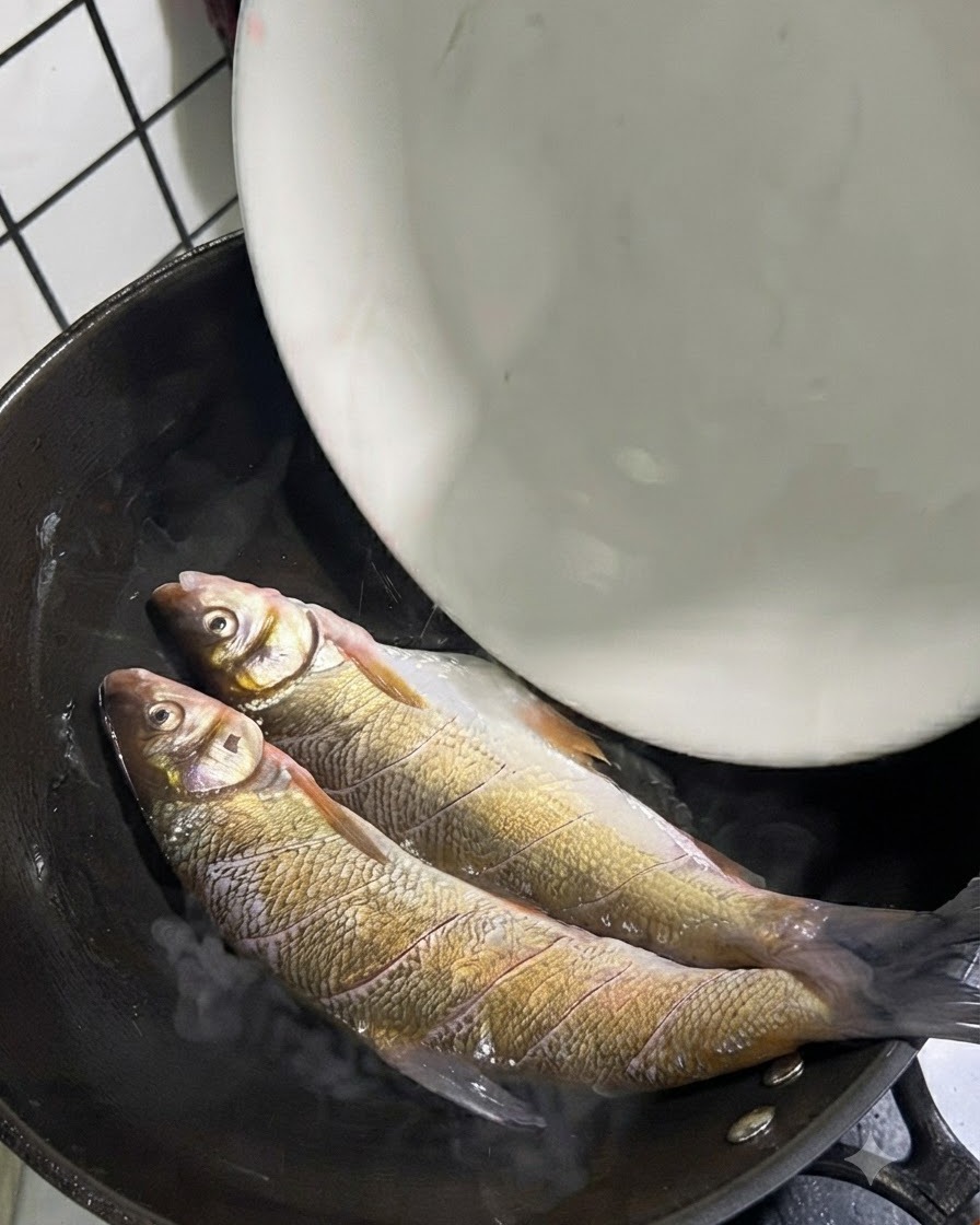 Dos pescados enteros de cola amarilla colocados dentro de un wok caliente con aceite.