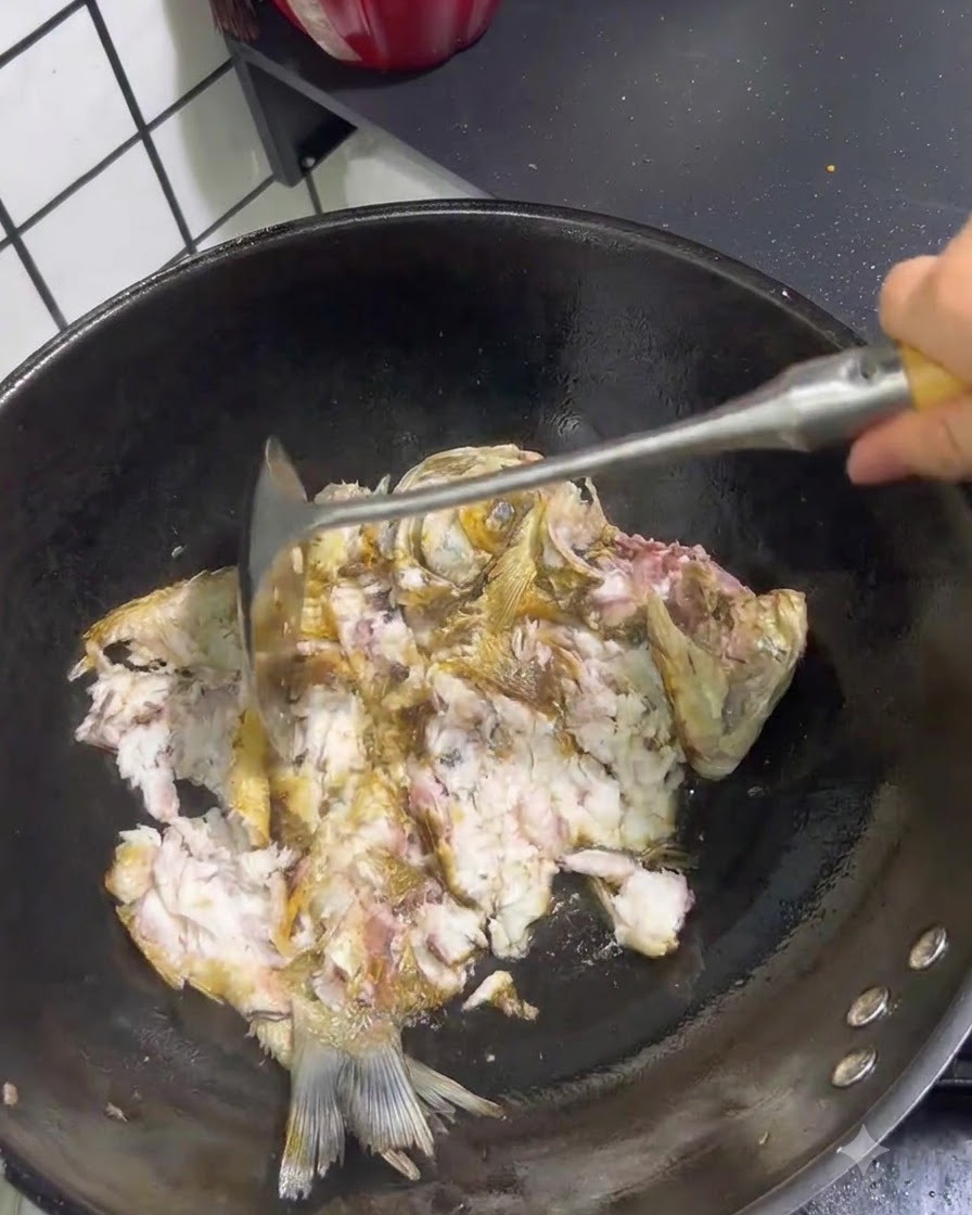 Pescado frito siendo deshecho y triturado con una espátula de metal dentro de un wok.