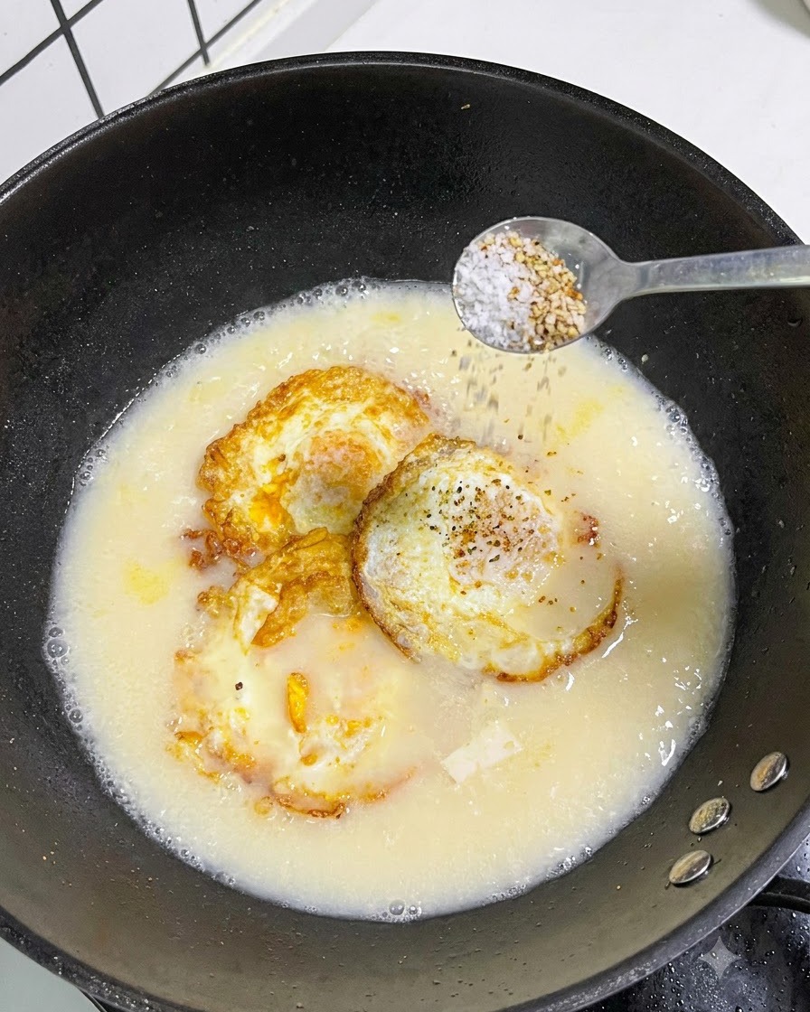 Una cucharada de sal y pimienta blanca siendo esparcida desde una cuchara en una olla de sopa.