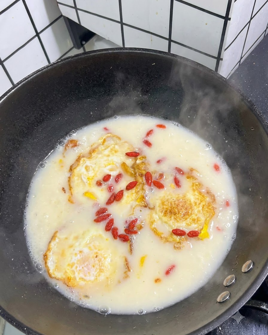 Bayas de goji rojas deshidratadas esparcidas sobre la superficie de una sopa blanca hirviendo con huevos fritos.