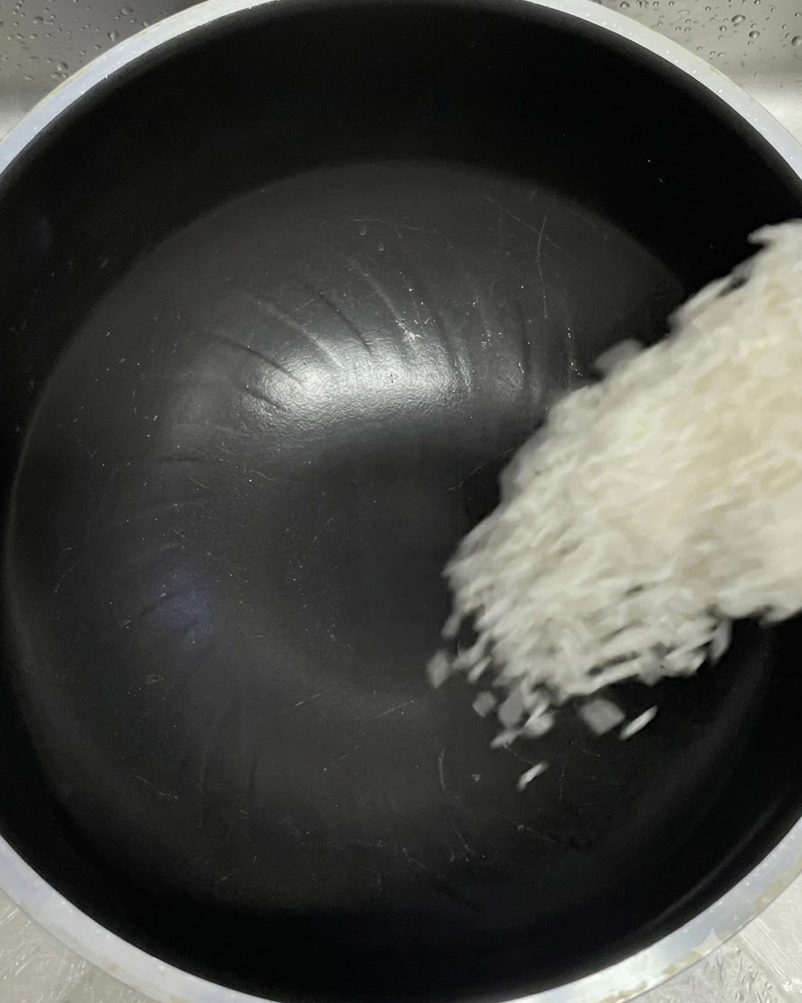 Granos de arroz blanco cayendo de una taza medidora en la olla interna negra de una arrocera.