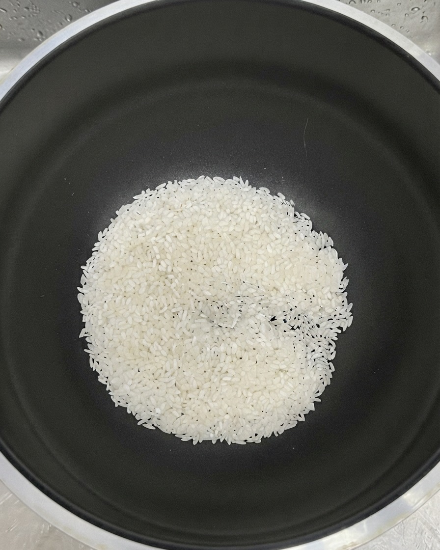 Arroz blanco en el fondo de una olla negra con agua para enjuagar.