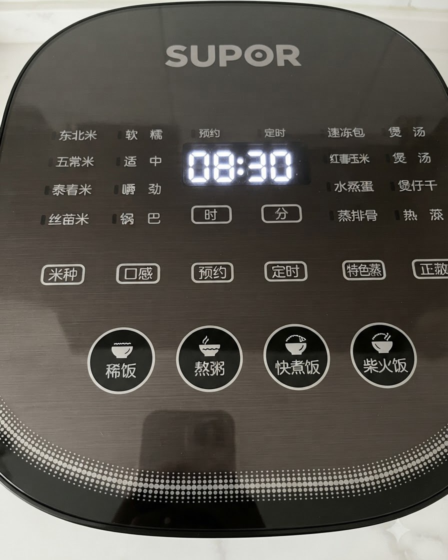 Vista de cerca de una mano presionando los botones en el panel de control digital de una arrocera negra mostrando la hora.