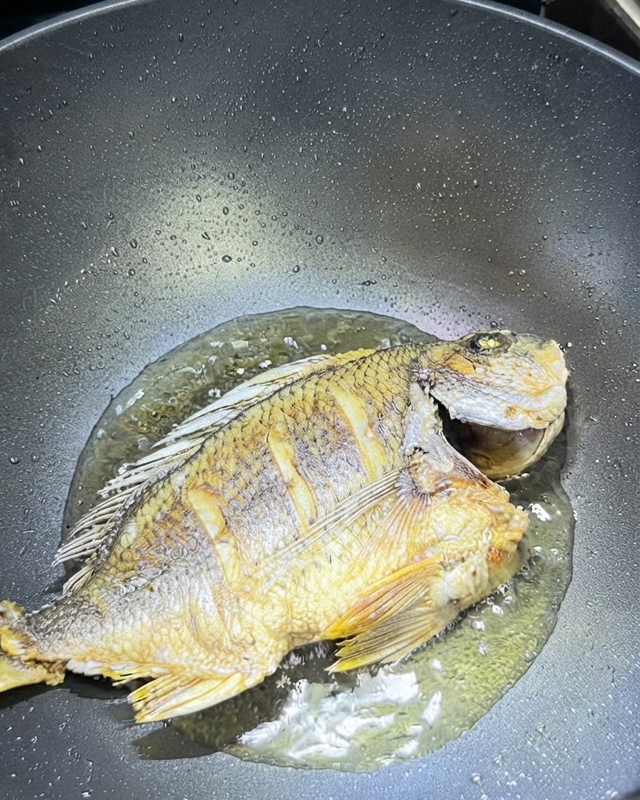 Rodajas de jengibre y ajo esparcidas alrededor del pescado frito en un wok.