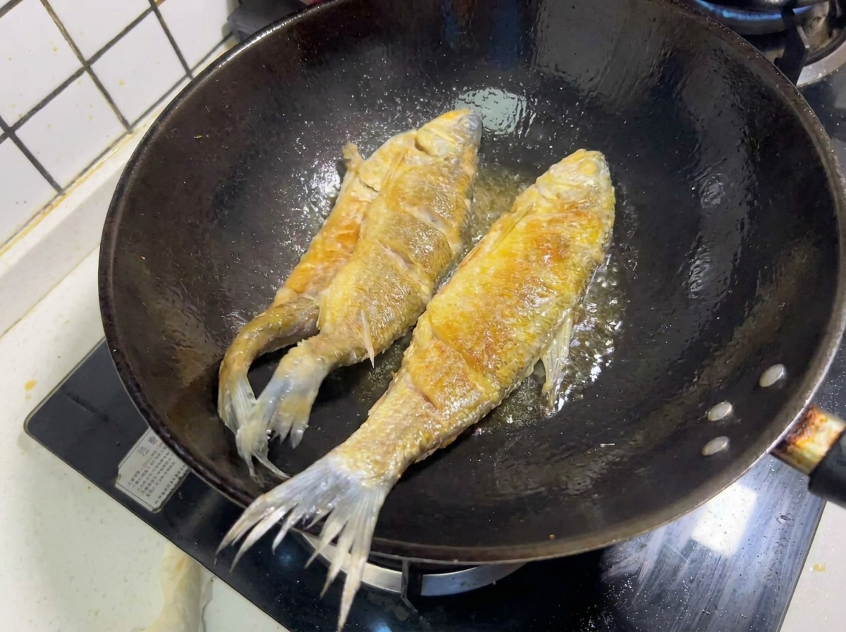 Dos pescados enteros friéndose en aceite caliente en un wok, mostrando una costra dorada y crujiente.