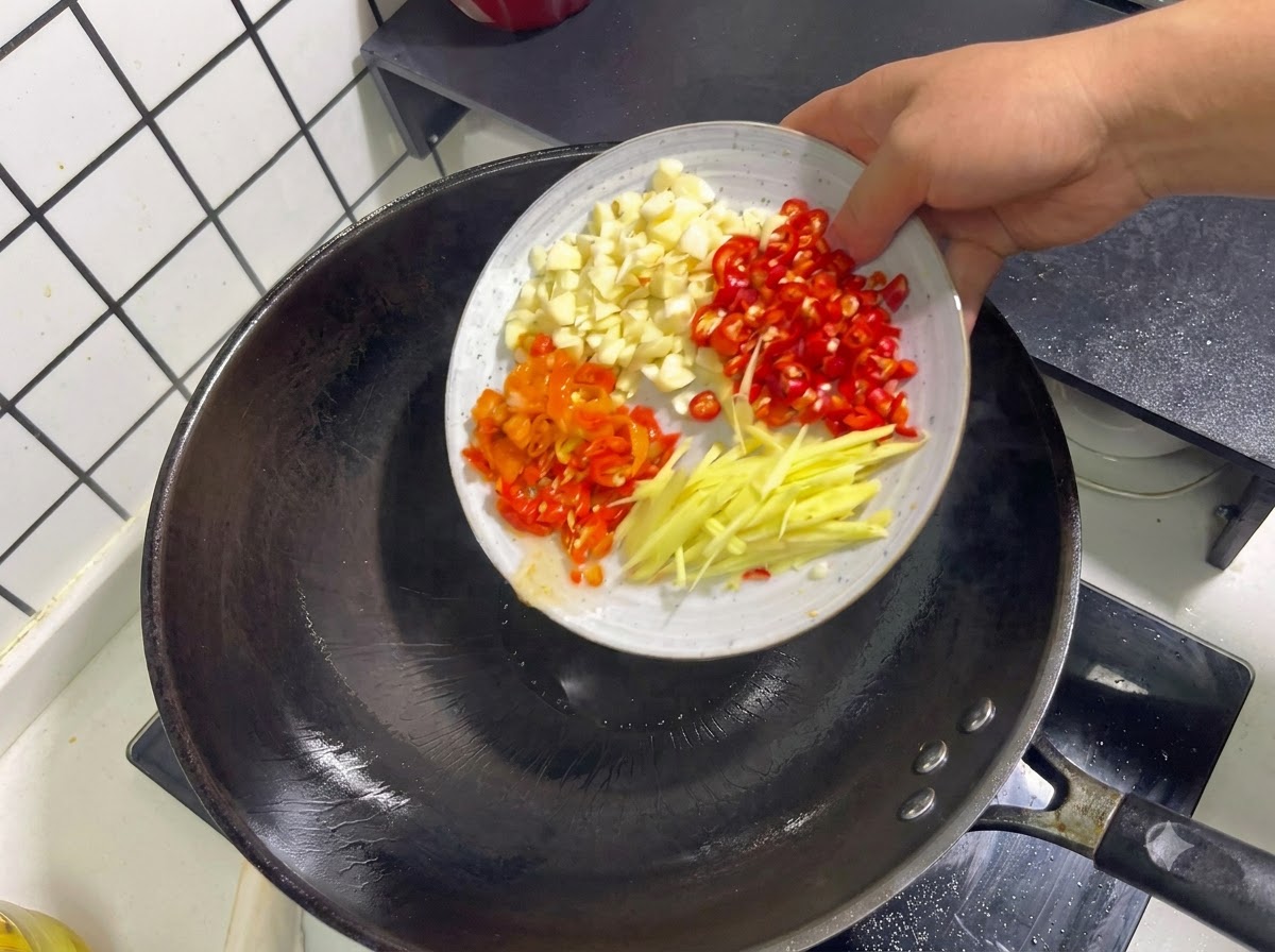 Ajo picado, chiles rojos, chiles en escabeche y tiras de jengibre siendo arrojados a un wok.