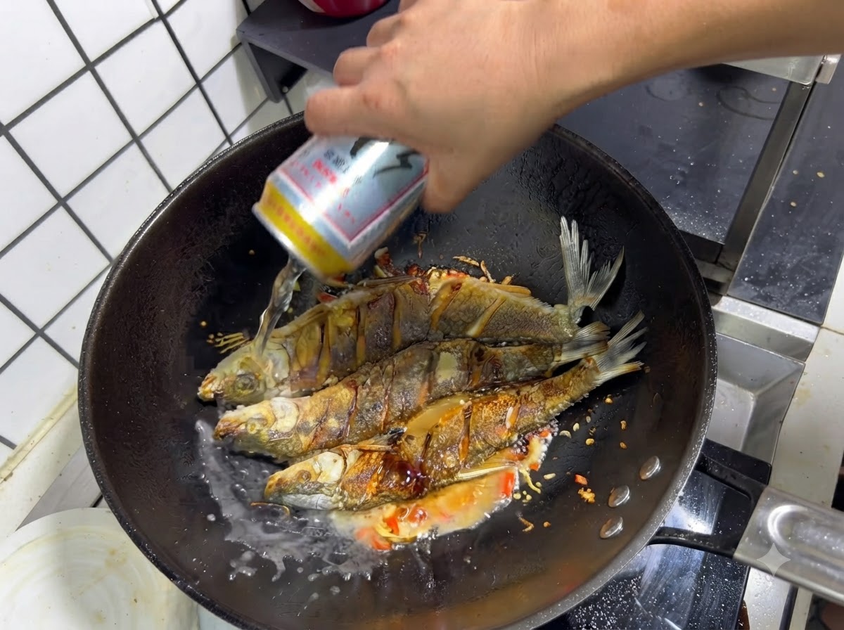 Una mano vertiendo una lata de cerveza en un wok sobre el pescado frito sazonado y los aromáticos salteados.