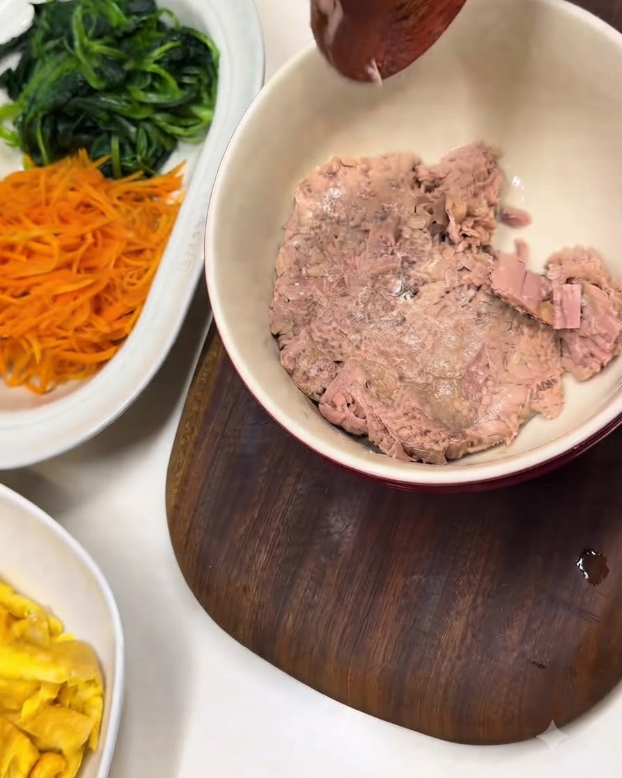 Un bol de atún en lata desmenuzado junto a un plato blanco con espinacas y zanahorias preparadas.