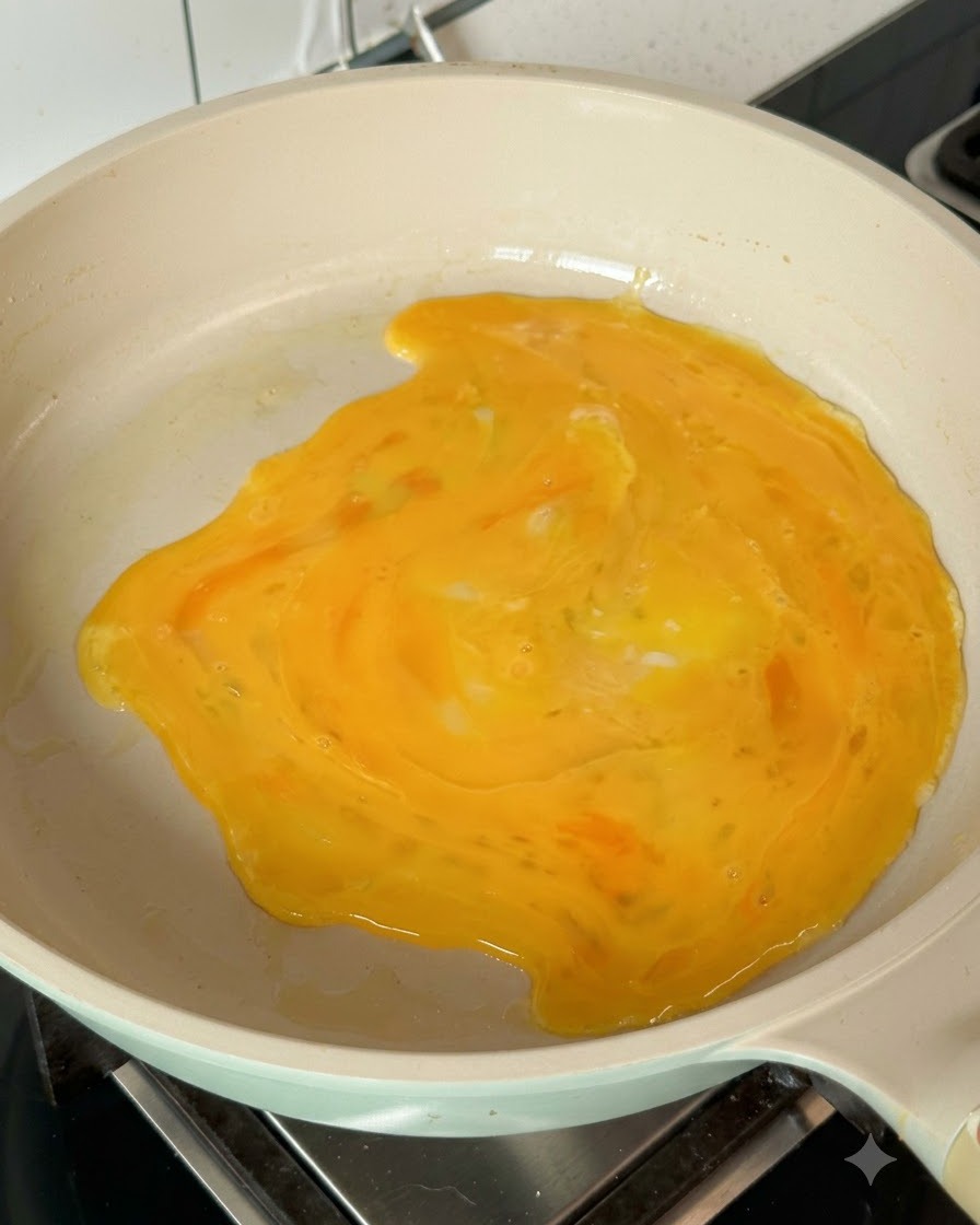 Huevos batidos extendiéndose por la sartén caliente para formar una tortilla fina.
